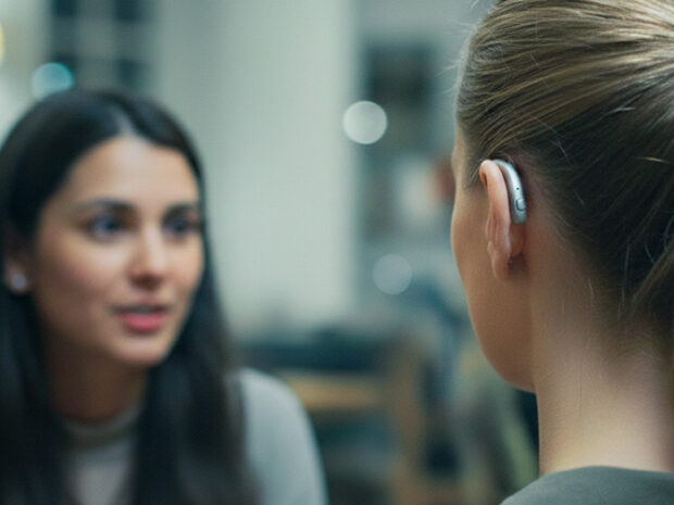 Mujer con audífono conversando con otras personas en un restaurante ruidoso